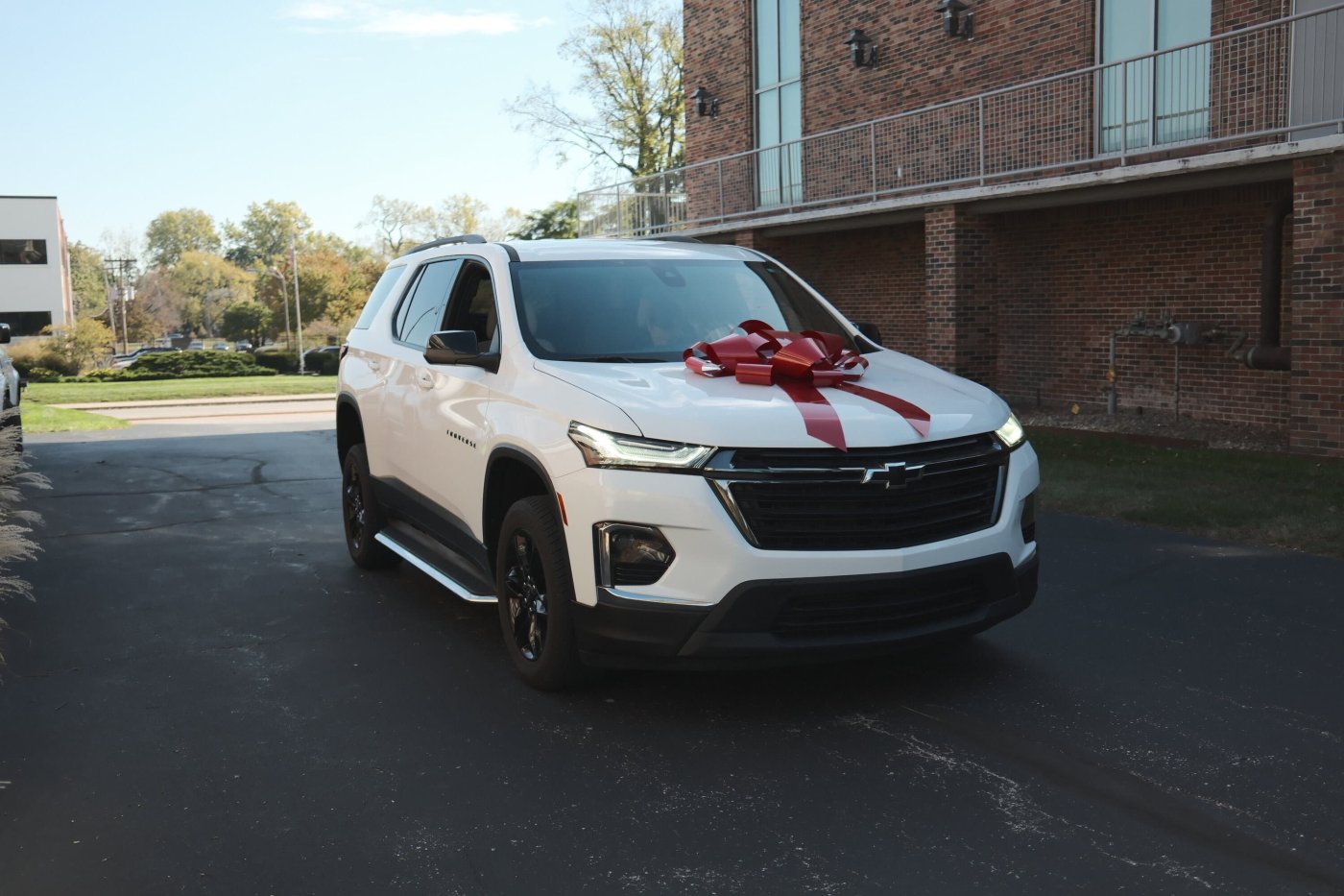 A white Chevrolet Traverse with a large red bow on the bonnet, parked outside Keller & Keller’s Indianapolis office
